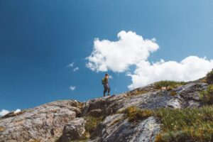 Low angle shot of a male with a backpack standing on the edge of the mountain under cloudy sky Low angle shot of a male with a backpack standing on the edge of the mountain under cloudy sky